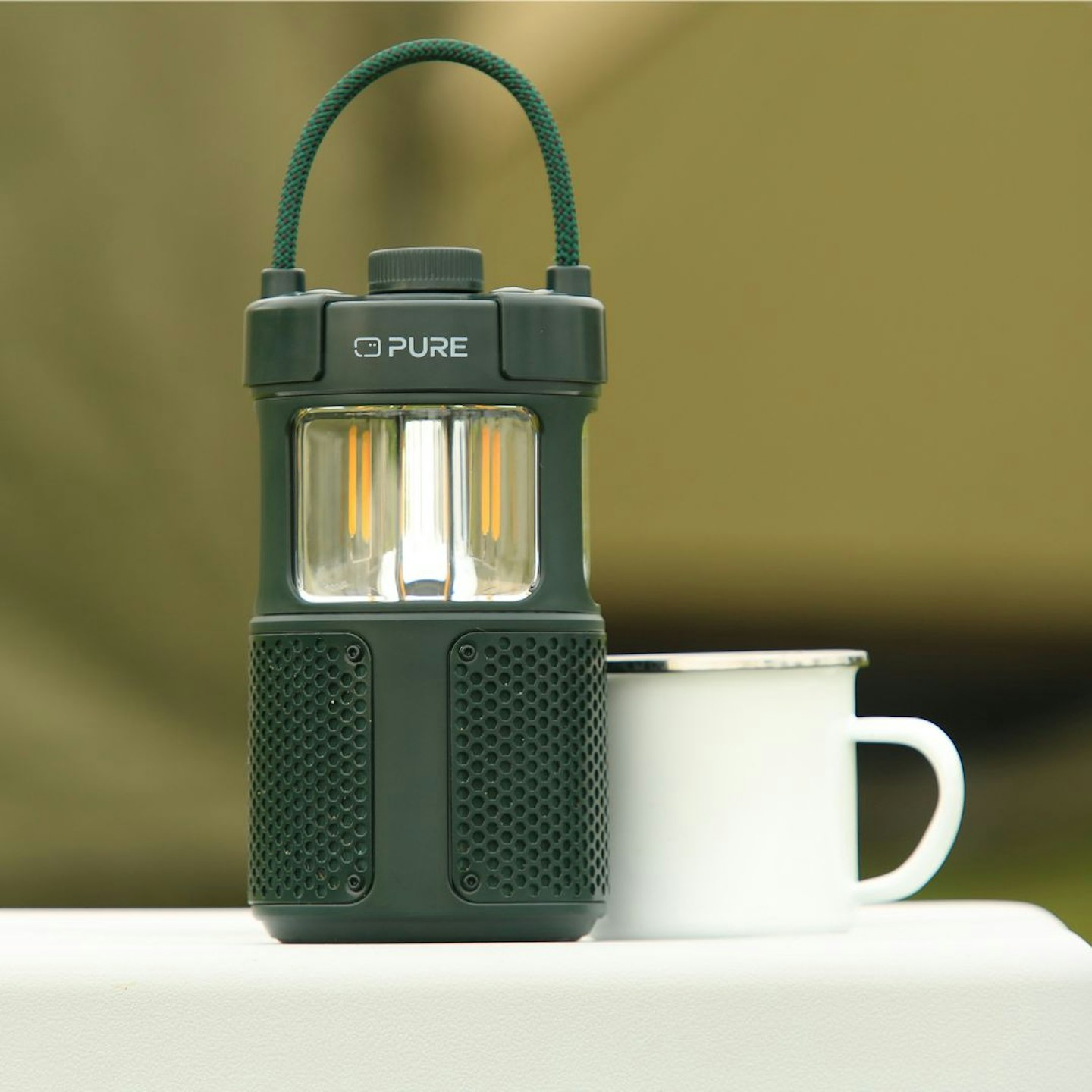 Pure Woodland Glow Outdoor Speaker sitting on a cool box next to an enamel mug