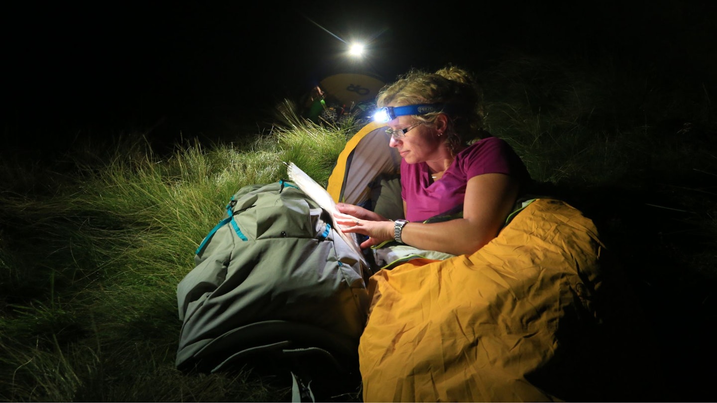 Hiker in their sleeping bag reading at night by using a head torch