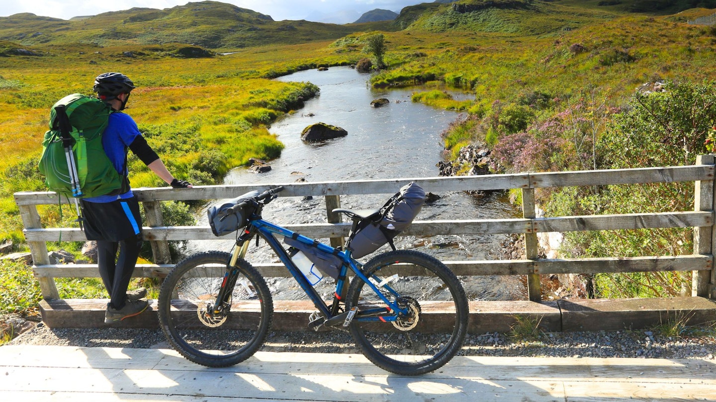 Cyclist stopping on a bridge during a bikepacking trip in Scotland