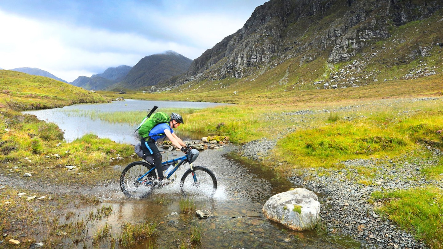 Cycling through a stream while on a bikepacking trip in Scotland