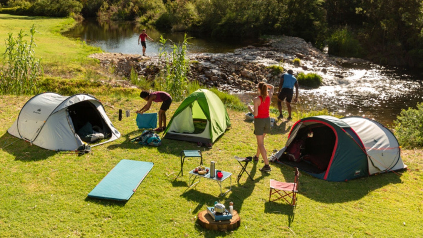 Three tents set up at a campsite by a river
