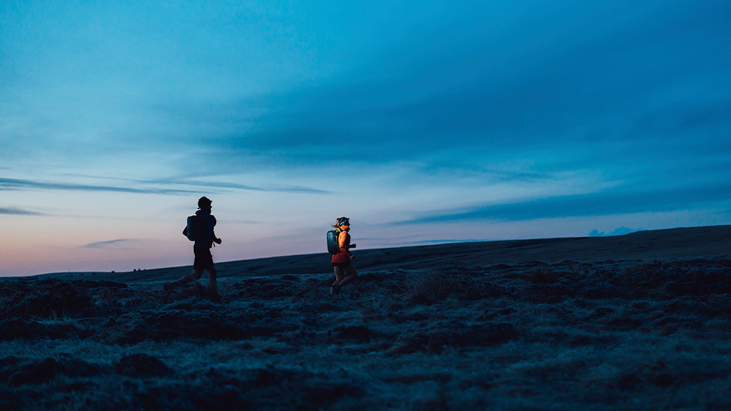 two runners with backpacks in the dark