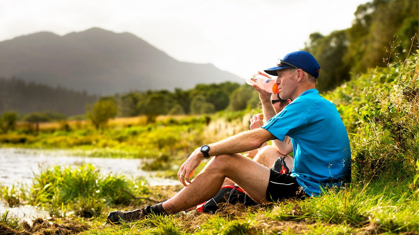 runner sits down with water bottle by a lake