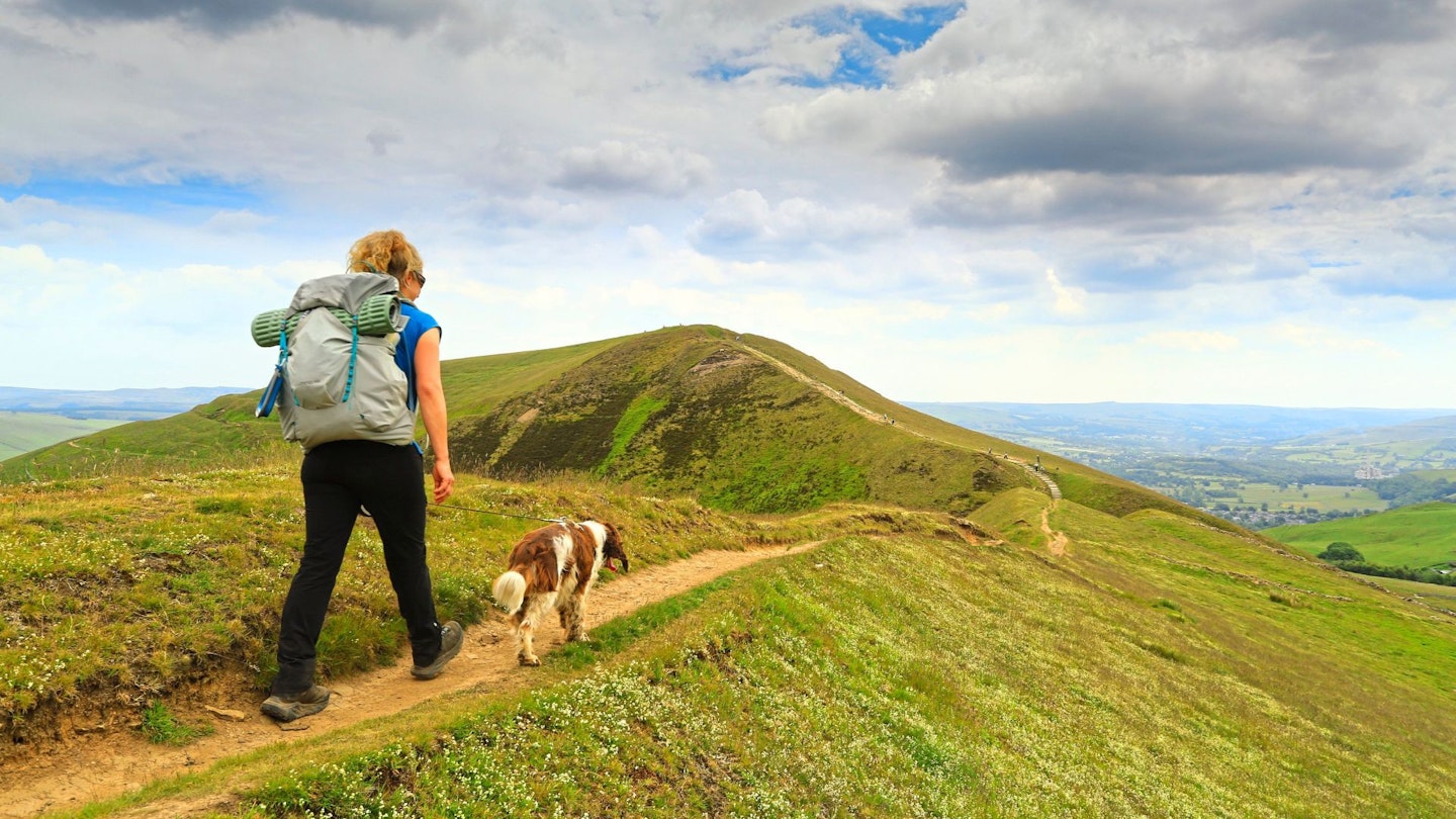 Female hiker carrying an overnight pack and walking with her dog in the hills