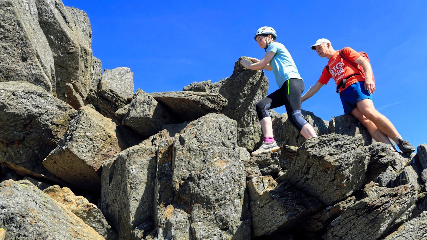 Hiker scrambling with their child on Crib Goch