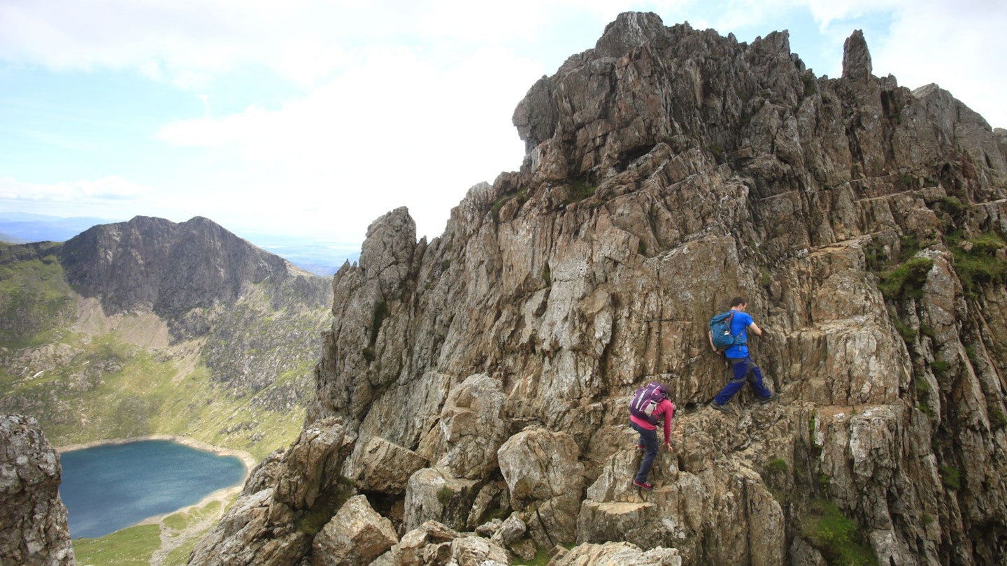 Two people scrambling on an exposed rock above a lake