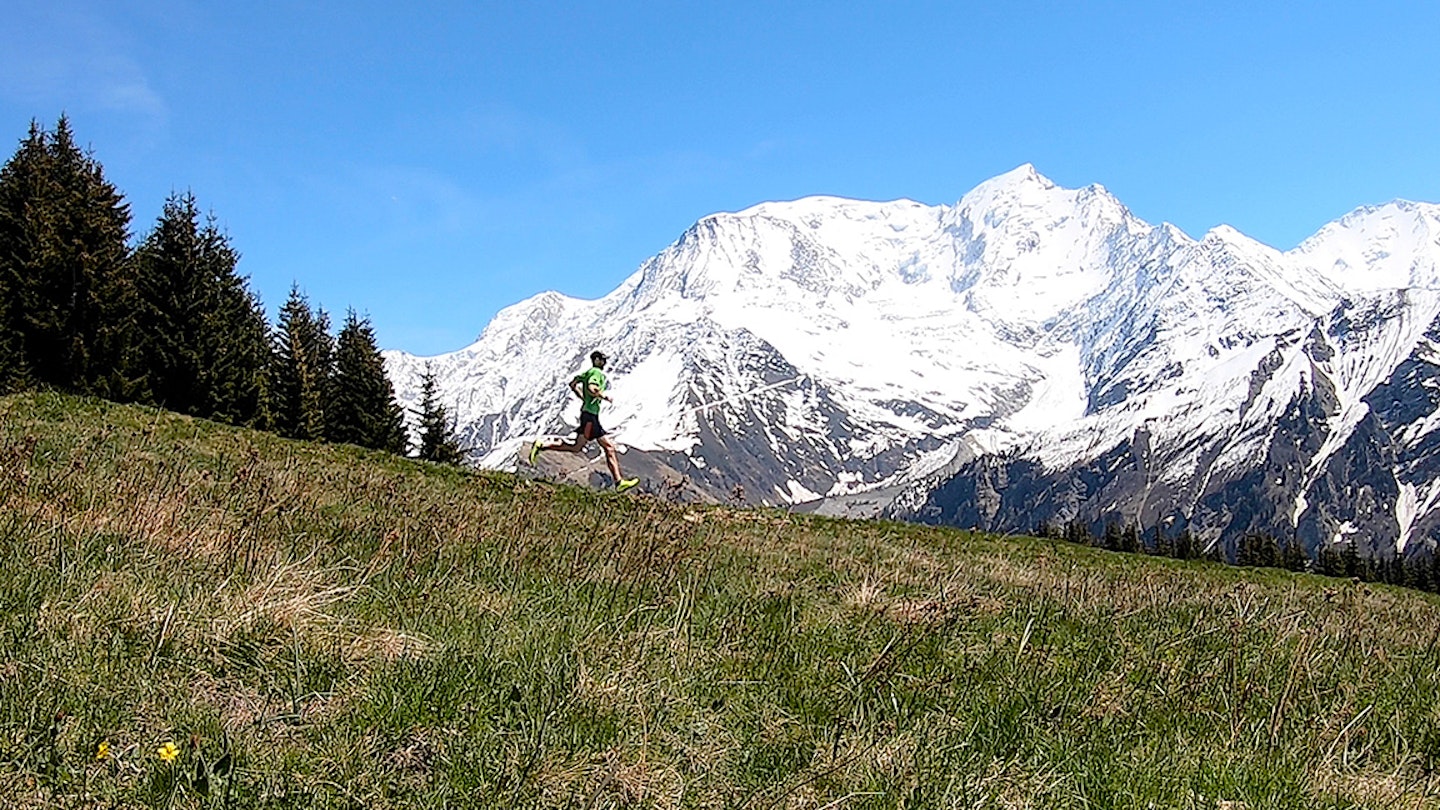 man runs down a field in the alps