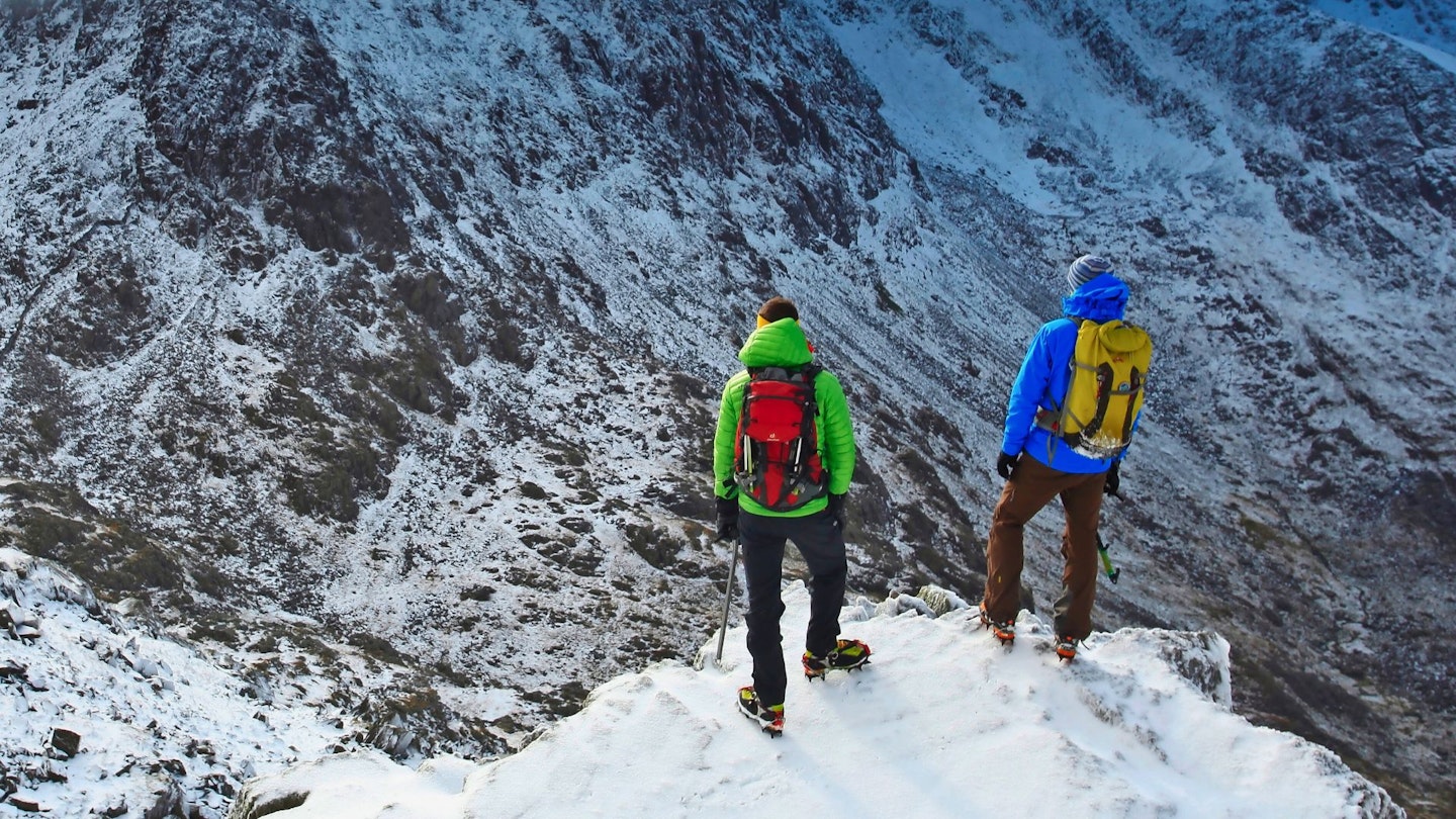 Hikers wearing mountaineering backpacks standing on a mountain ridge in winter