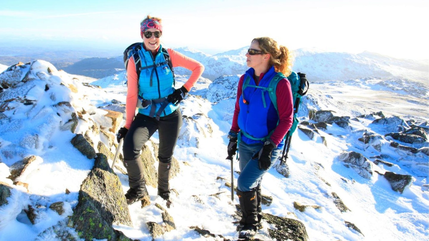 Two hikers on a snowy summit wearing sunglasses