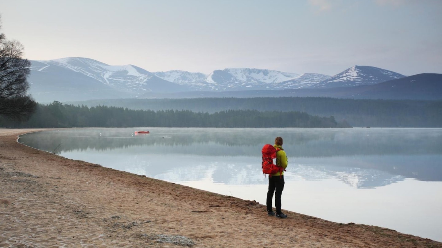 Hiker on Loch Morlich beach with the Cairngorm plateau beyond