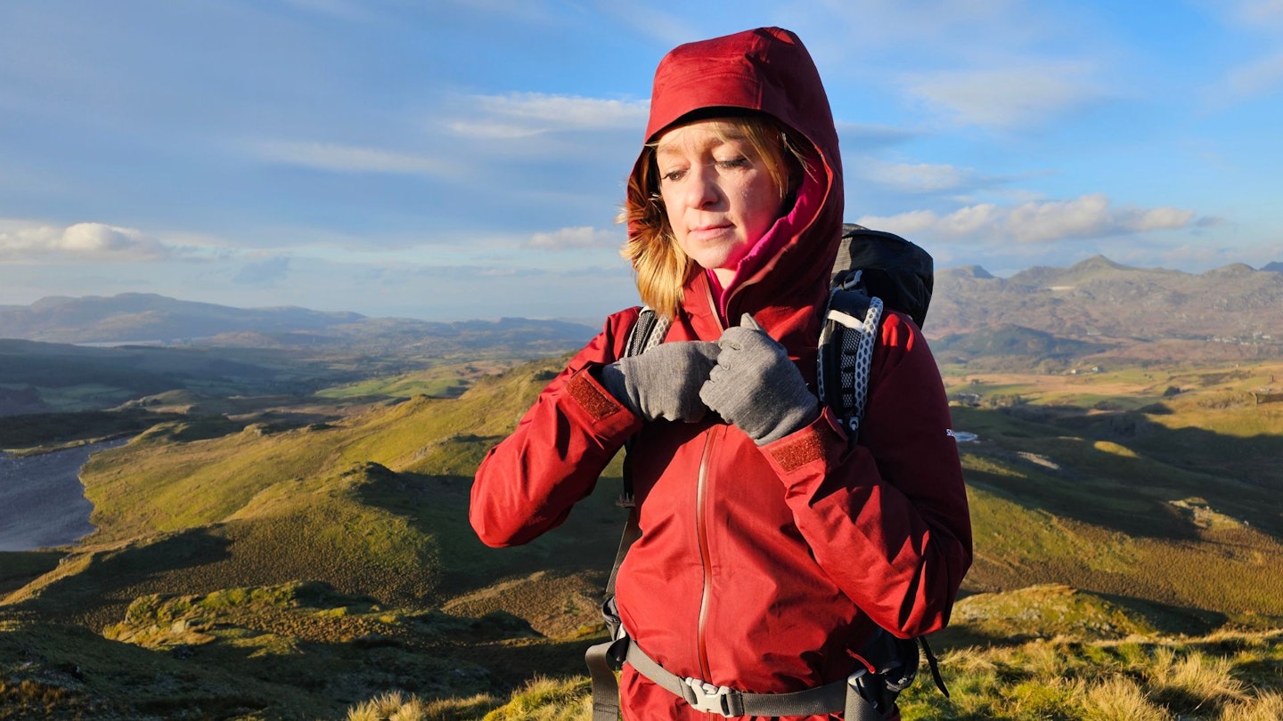 A woman stands on a summit in a Salewa Puez Paclite