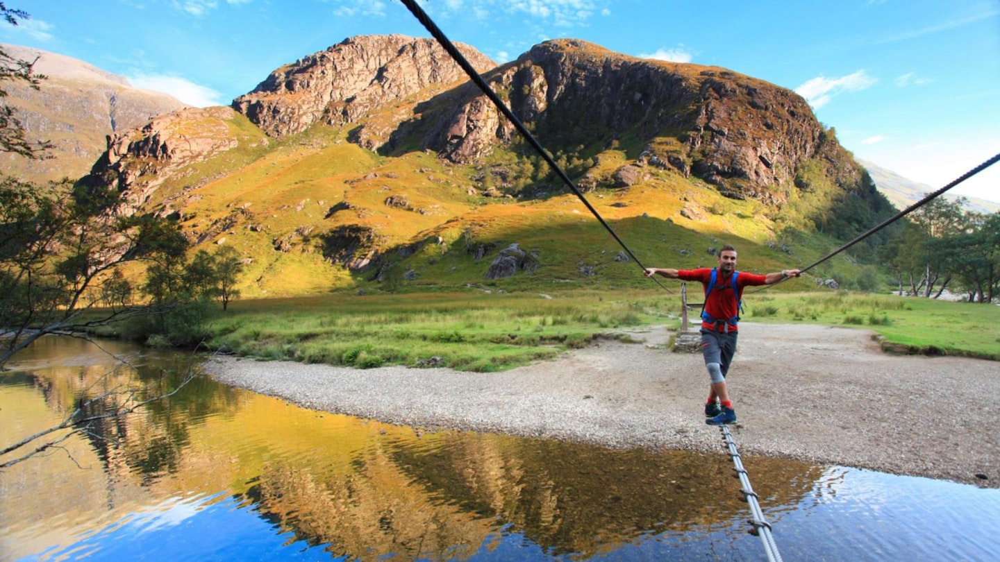 Hiker crossing the Water of Nevis bridge Ring of Steall Glen Nevis Scotland