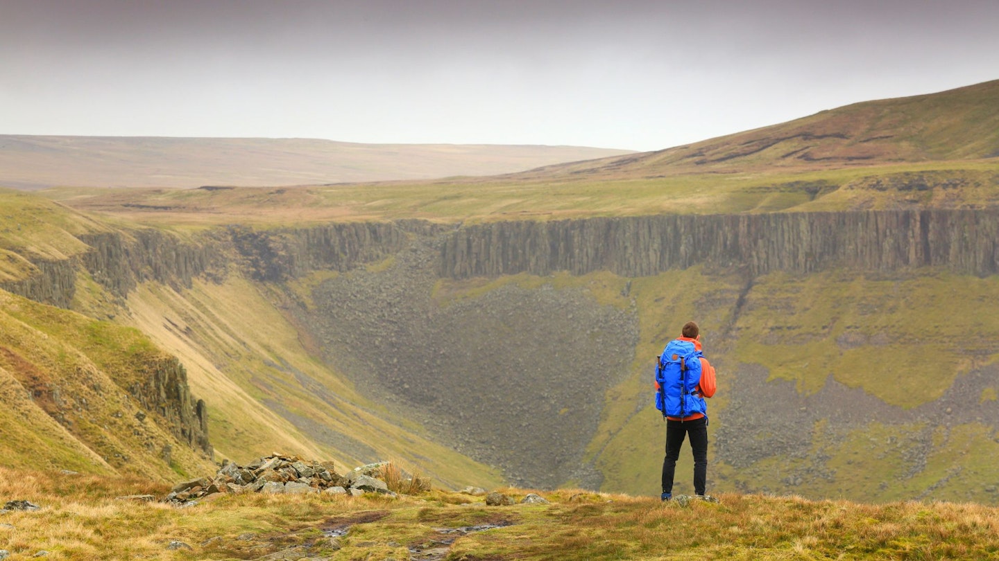 Chris Williams standing at top of High Cup Nick while testing the Fjällräven Kajka 55