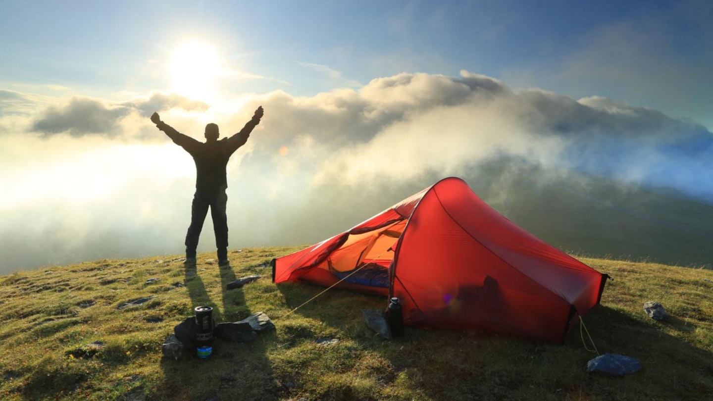 A man celebrates next to his backpacking tent in the sunset