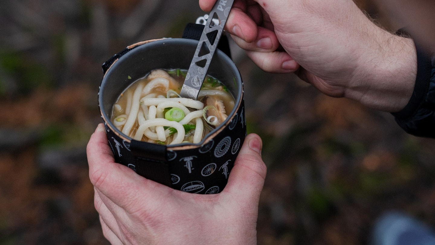 Wating a camping meal with a camping cutlery from a camping mug