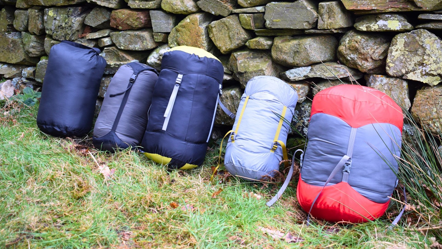 6 sleeping bags lined up along a wall compressed in their stuff sacks