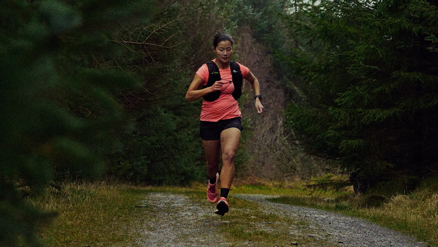 woman trail running in a pink tee shirt and inov8 trailfly shoes