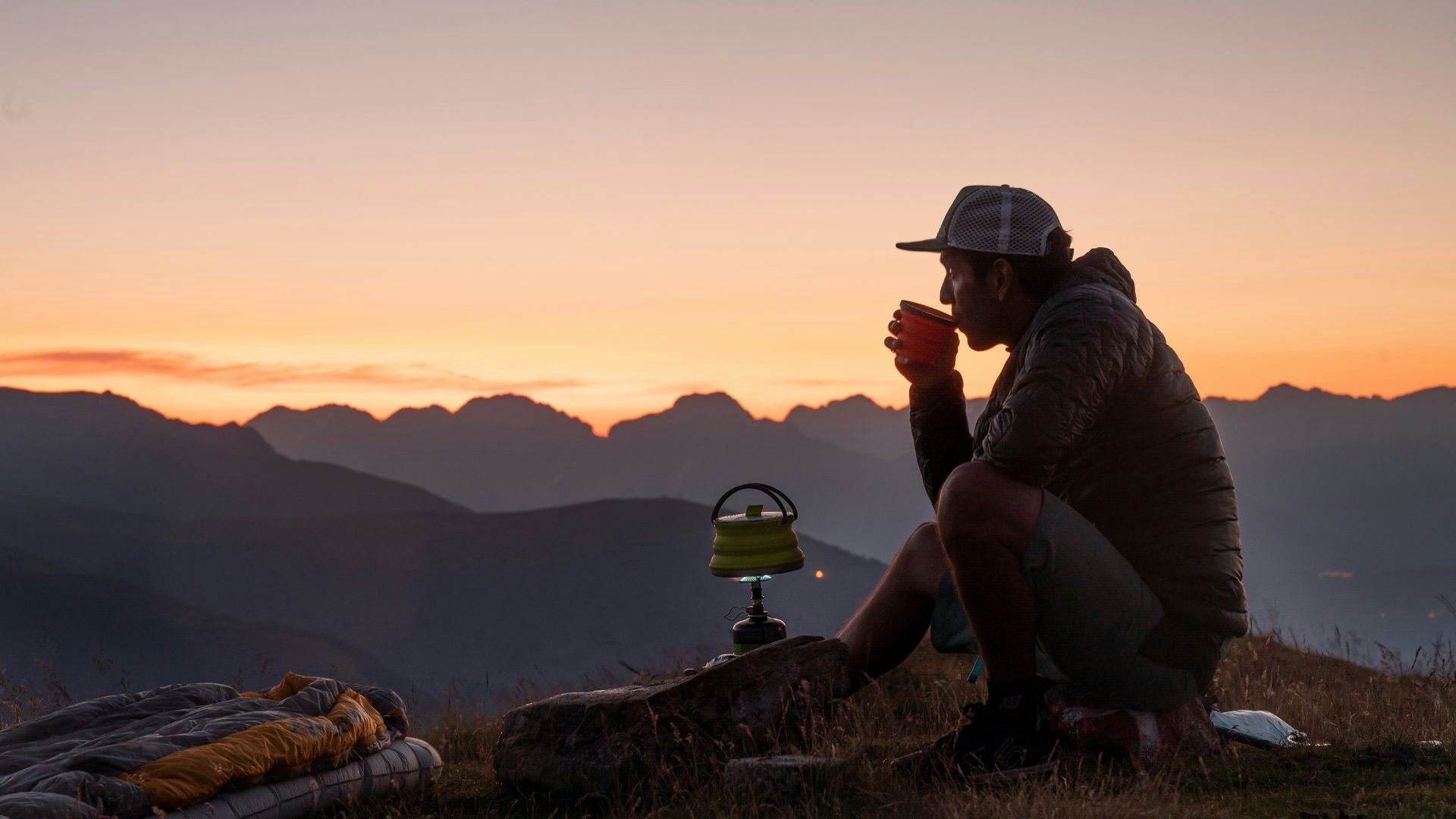 man sips coffee at sunrise over the mountains.