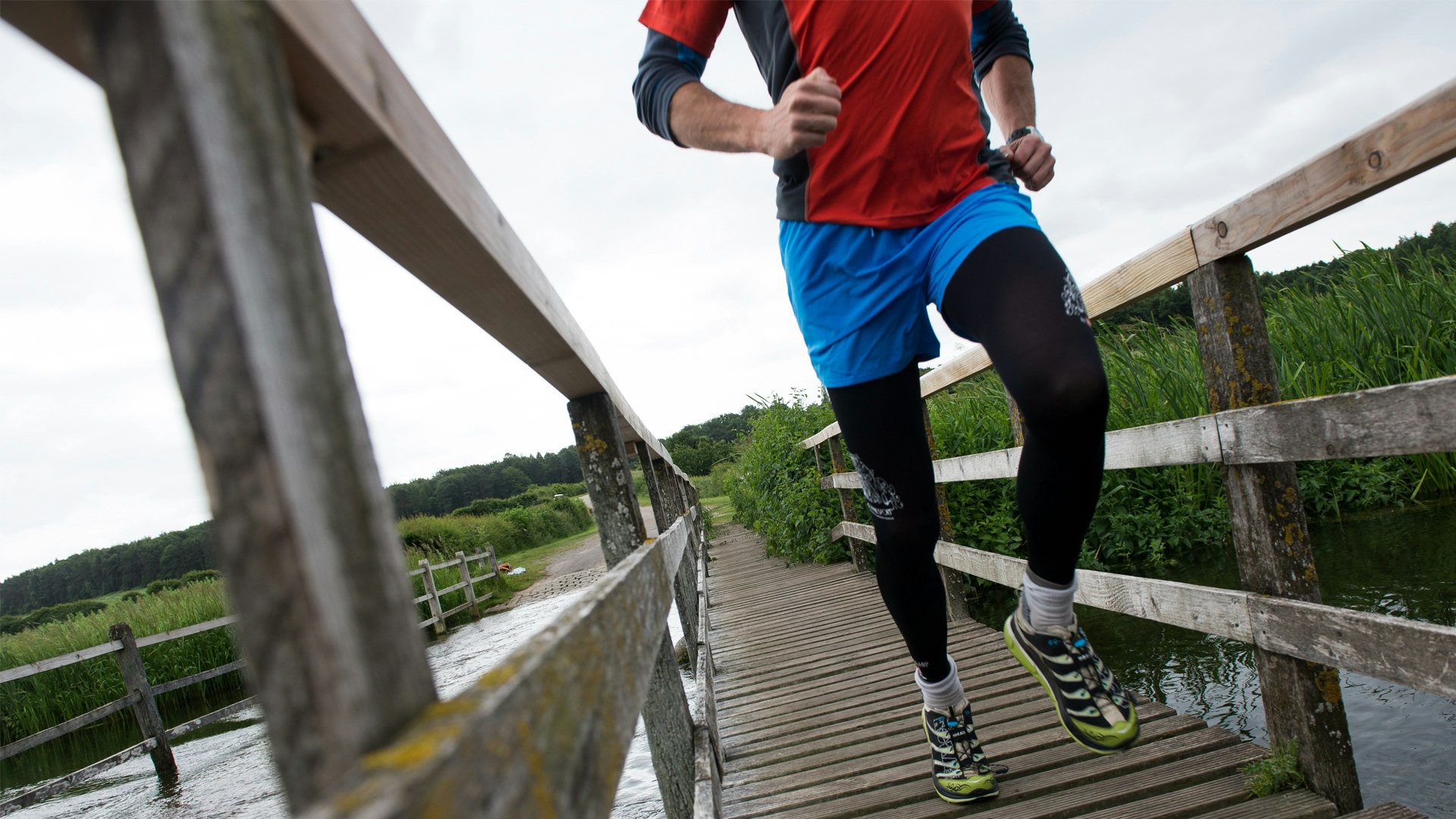 runner crossing a wood bridge with compression tights and hoka shoes