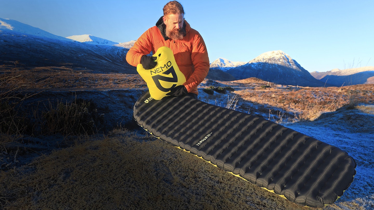 Man inflating Nemo sleeping mat with snowy mountain backdrop