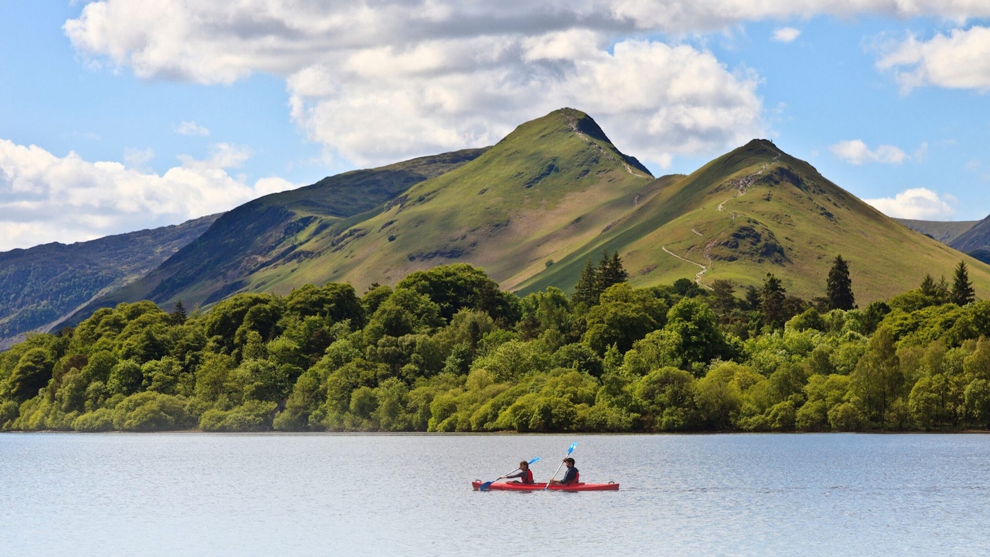 Two people paddle a red canoe on Derwent Water with Catbells in the background.