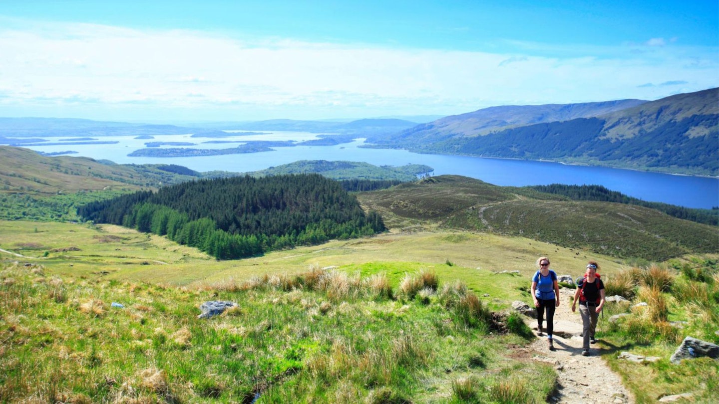 Fenale hikers climbing Ben Lomond with Loch Lomond behind in the Scottish Highlands