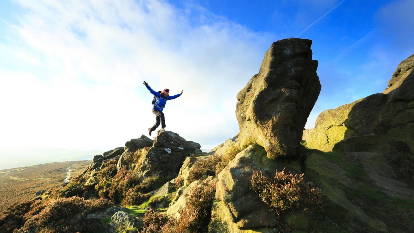 Hiker jumping on rocks near top of Win Hill Peak District