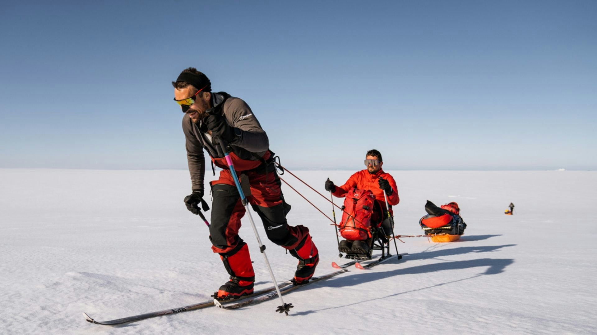 A man on skis pulling another man on skis across an ice cap