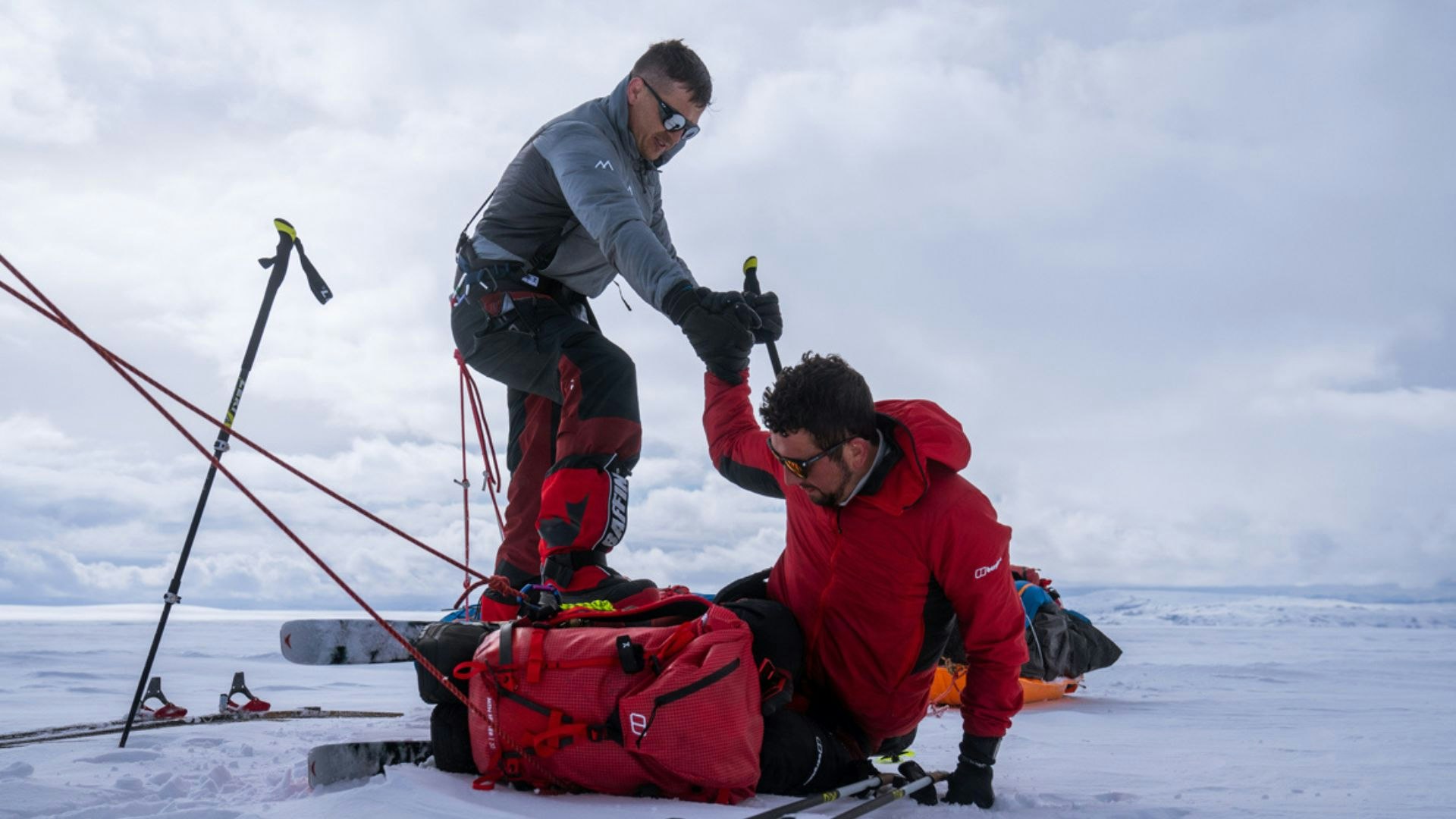 one man helping another man get up during a winter ski expedition