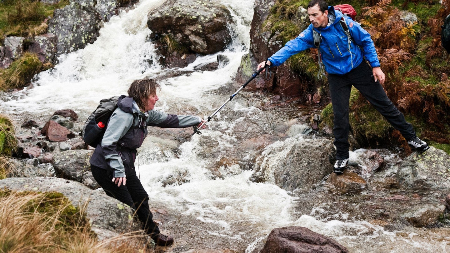 Kenton Cool helping a woman across a stream