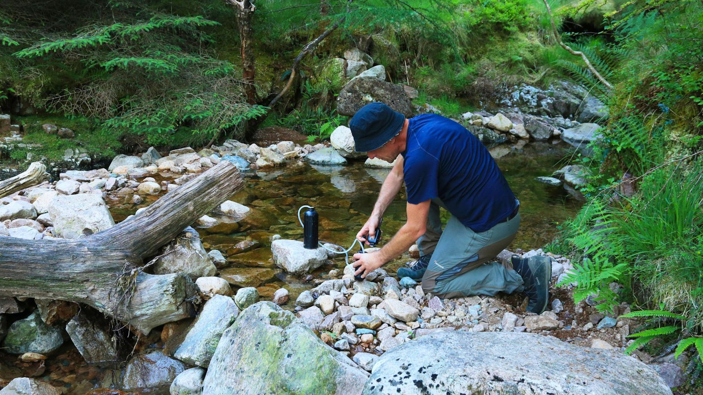 Hiker filtering water from a mountain stream using a water filter