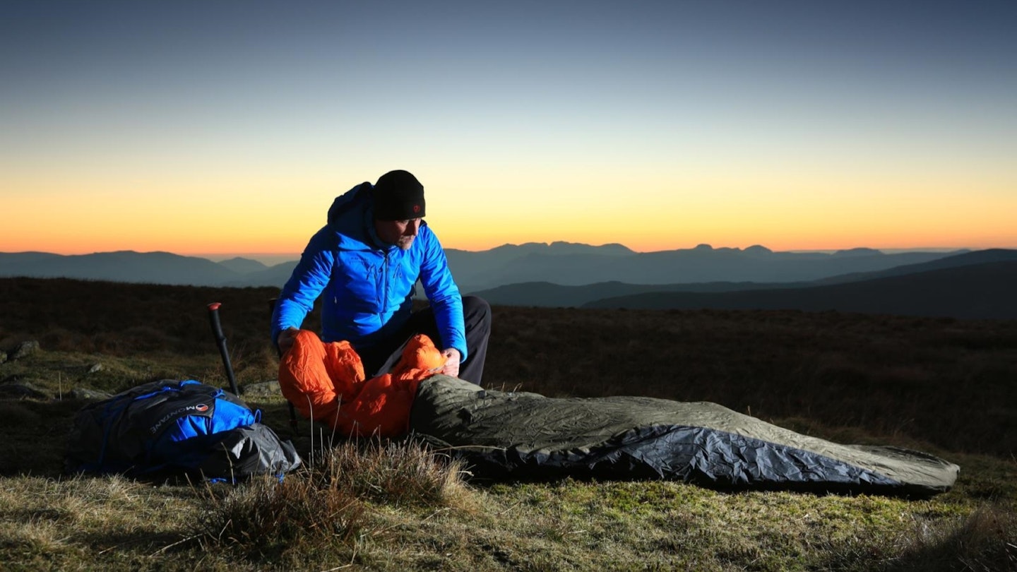 Hiker laying out a bivvy bag on the summit of Red Screes, Lake District