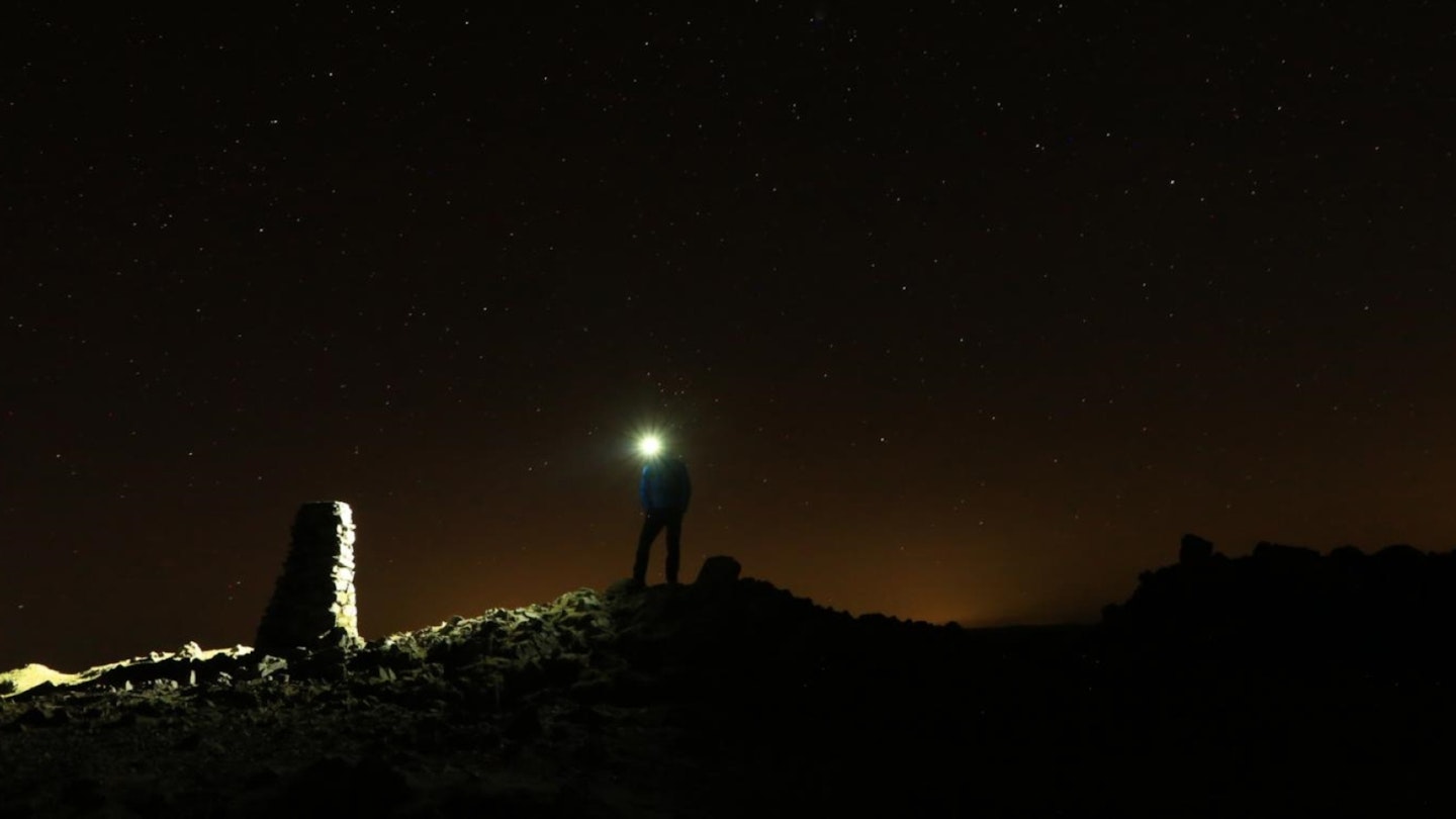 Hiker with a headtorch at the summit of Red Screes, Lake District