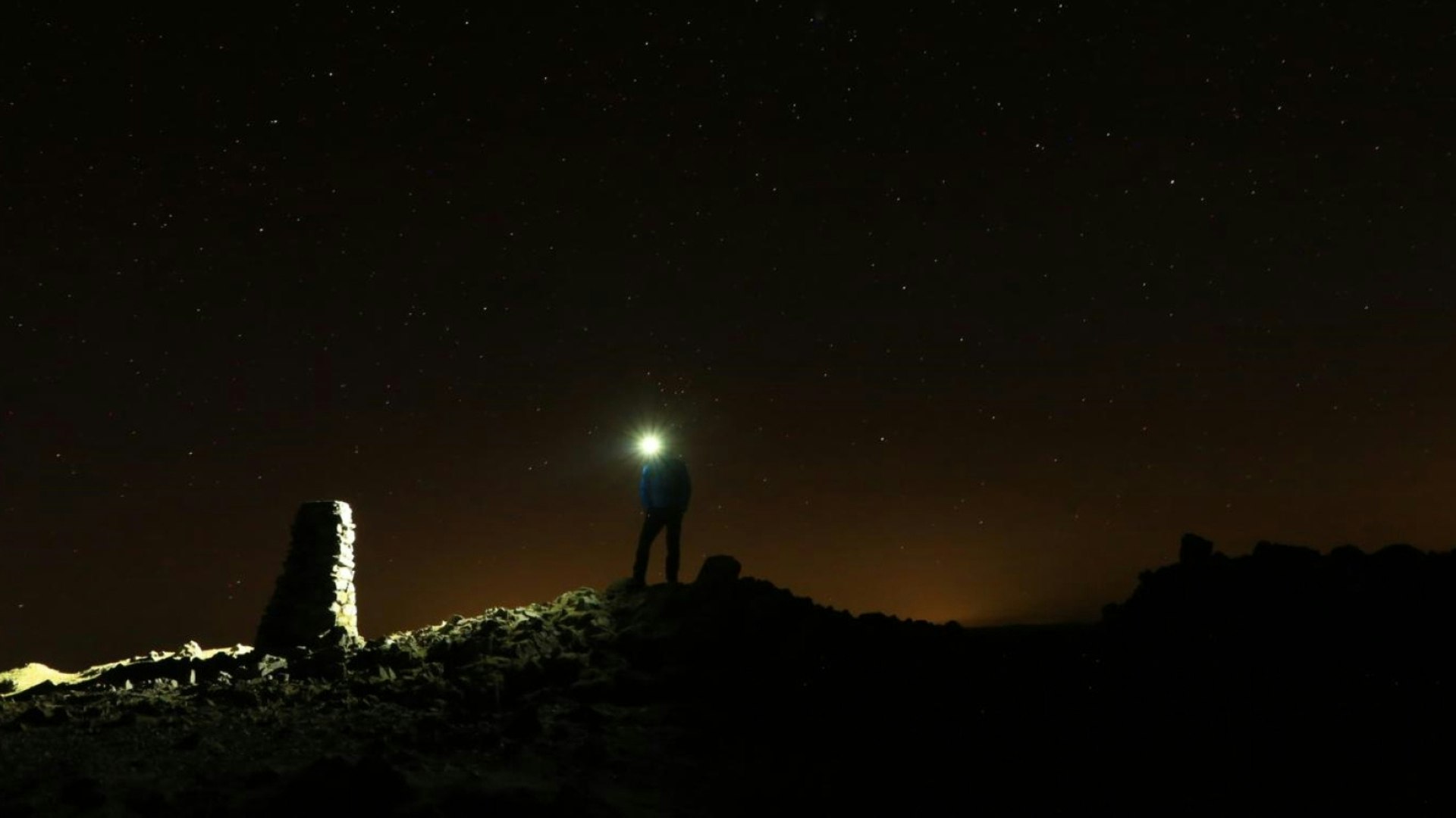 Hiker with a headtorch at the summit of Red Screes, Lake District