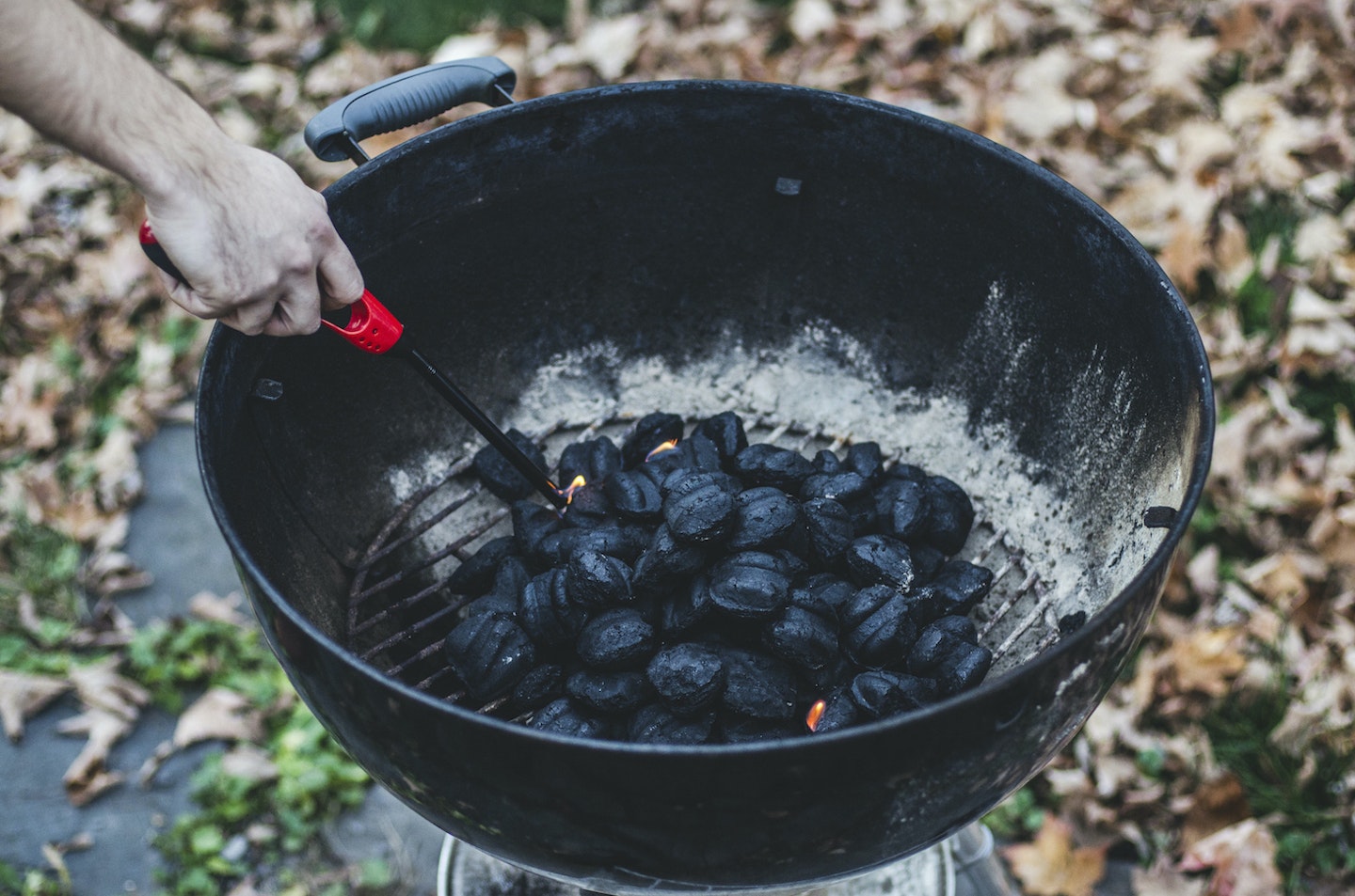 Hand Lighting Charcoal Grill with Autumn Leaves in Background