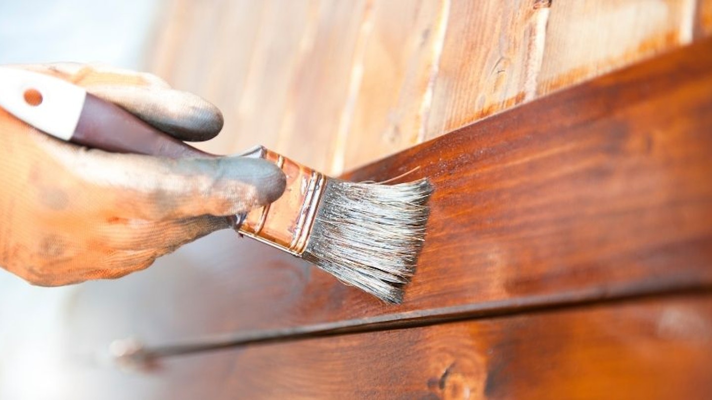A close up of a hand holding a brush and painting their shed