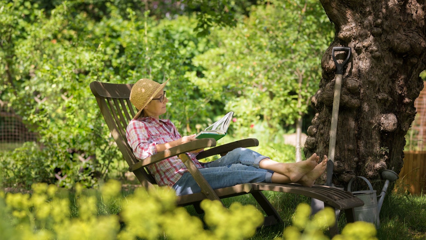 Senior woman in deck chair, relaxing in garden, under an old apple tree