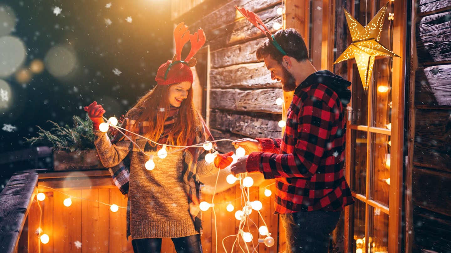 Happy couple outdoors putting up Christmas lights