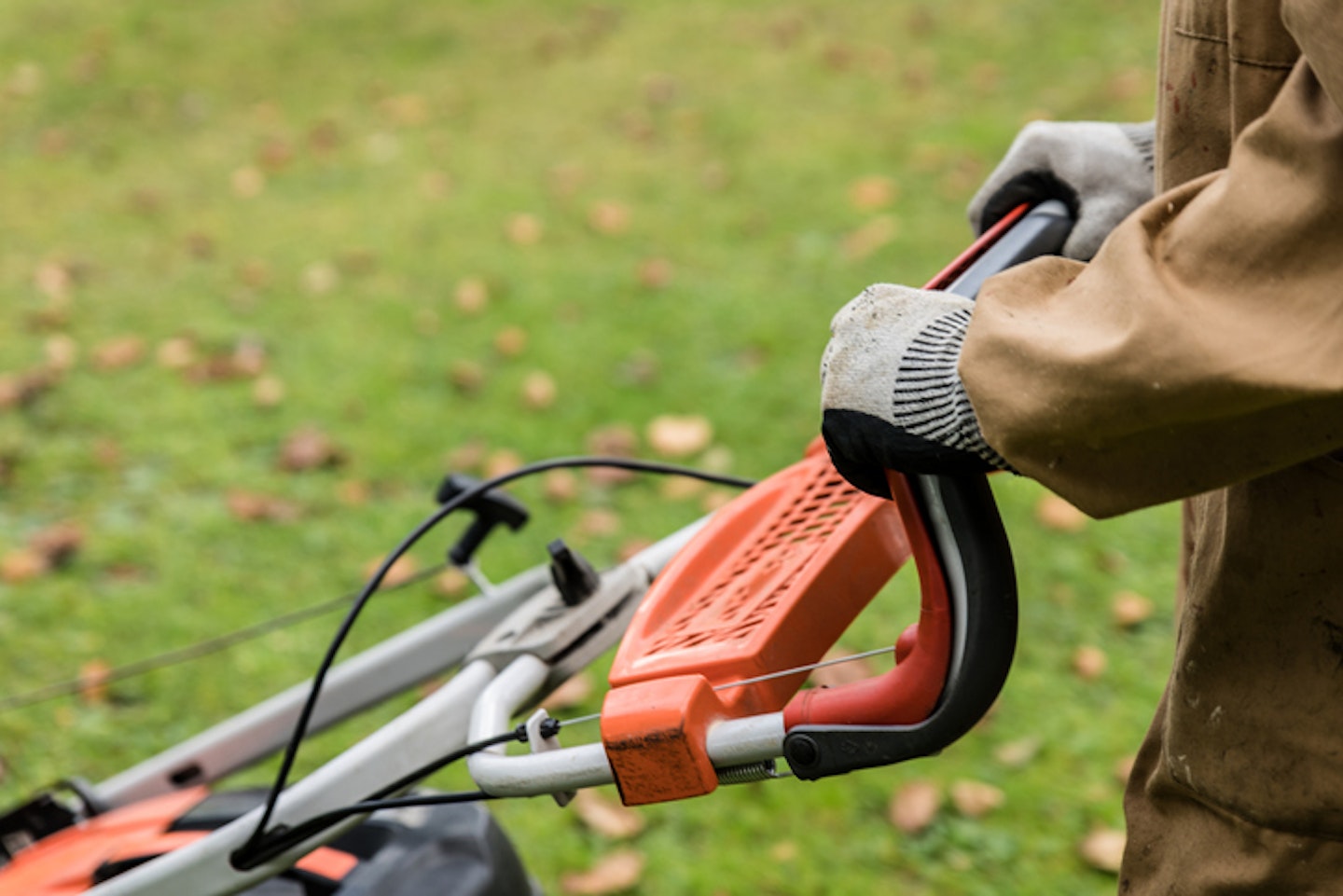 Close-up view of an unrecognizable gardener with gloves mowing the grass with a lawnmower.