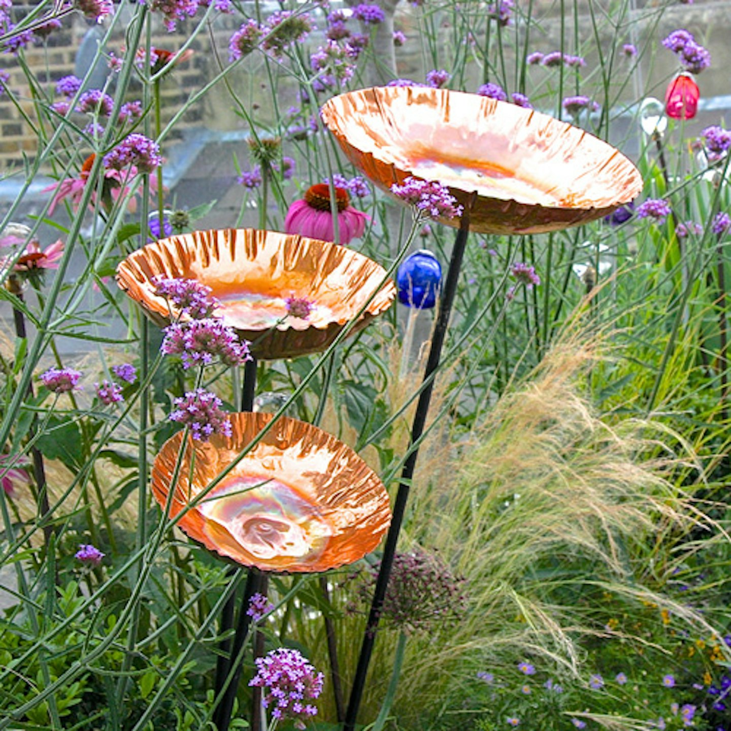 copper bird baths on stakes in flowerbed