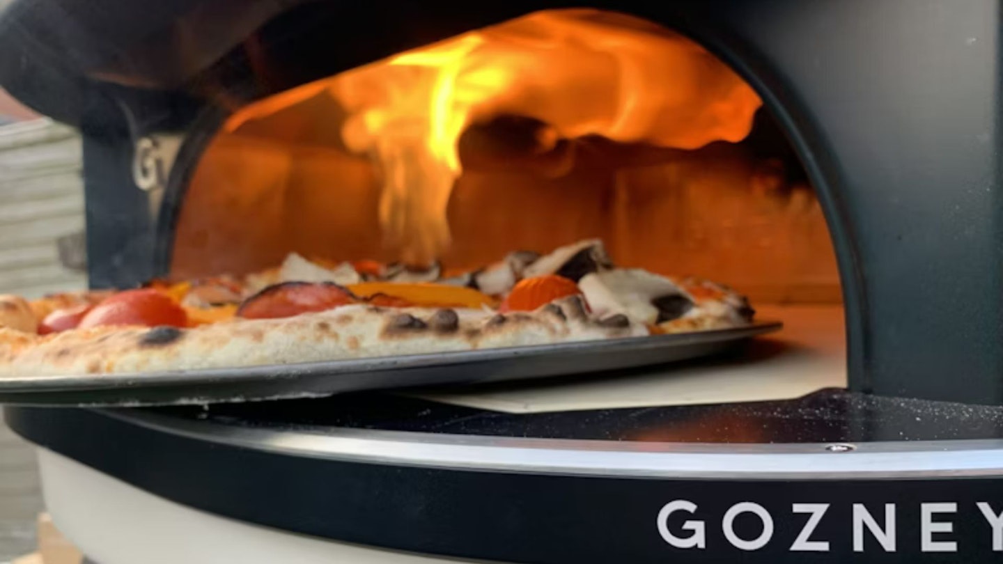 Wood-fired pizza coming out of a Gozney Dome Pizza Oven
