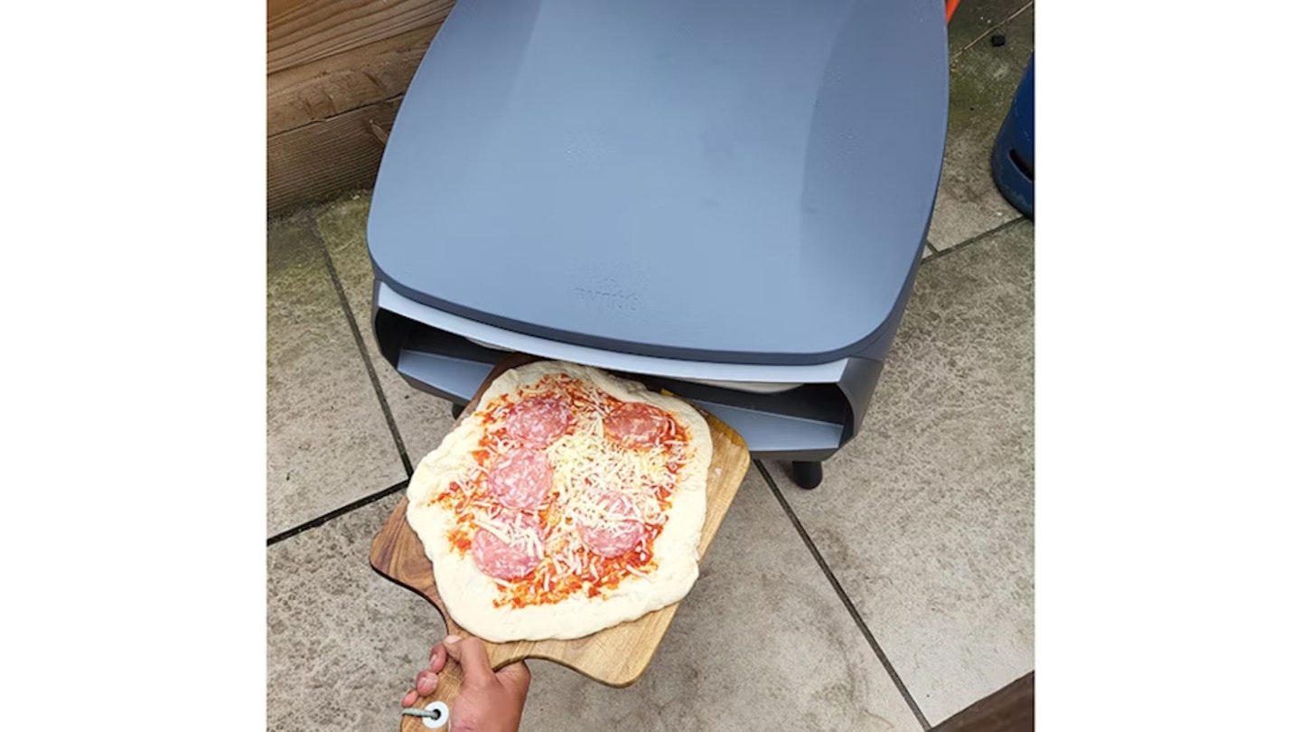 Putting an uncooked homemade pizza into the Witt Etna Fermo pizza oven