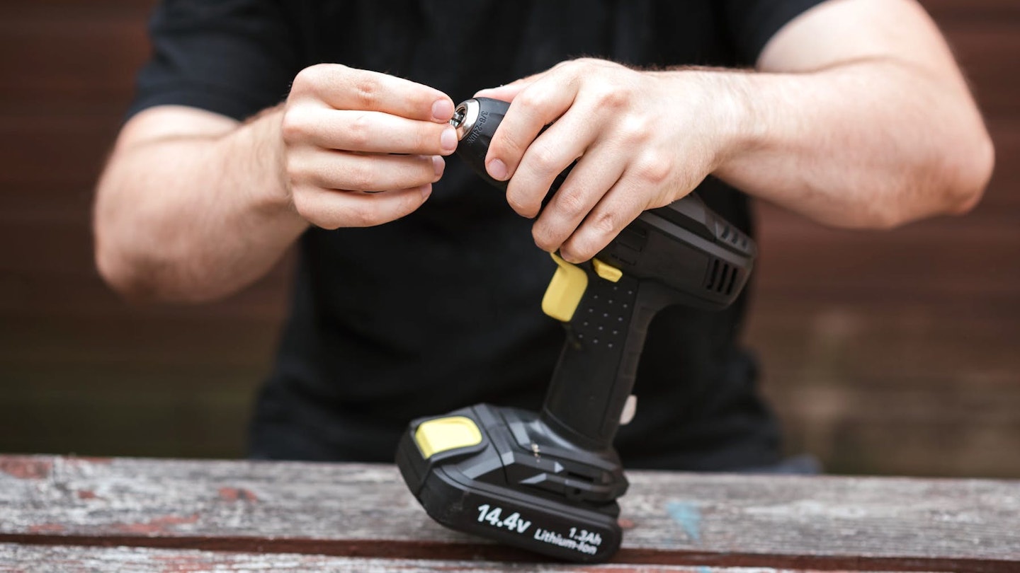 A cordless drill being set up by person at a bench