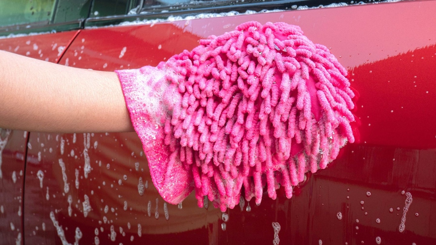 A pink wash mitt cleaning a red car