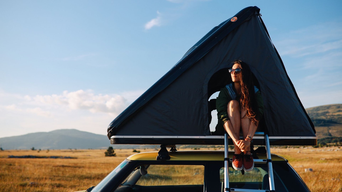 Woman sitting at the door of a rooftop tent