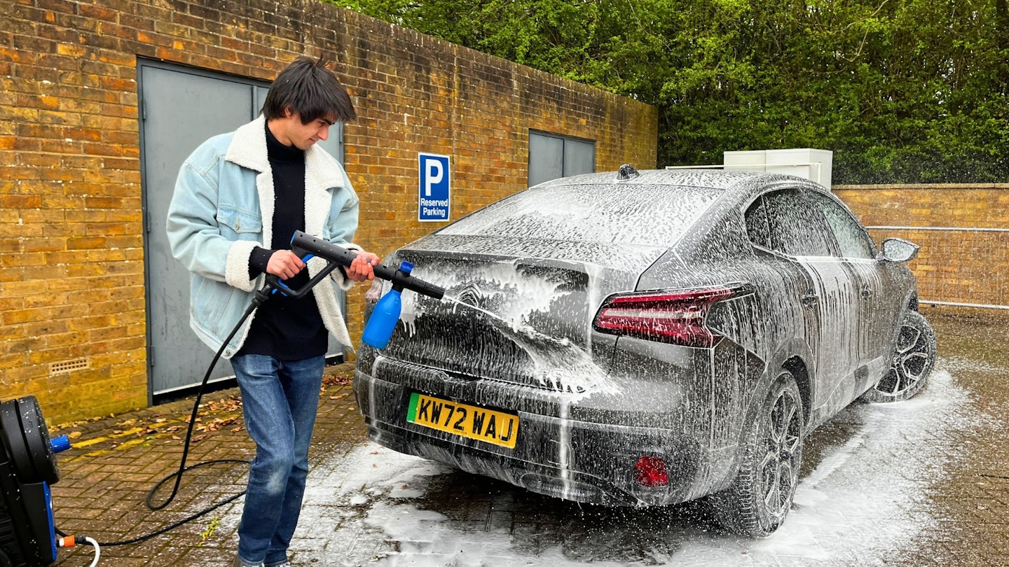 Aaron Hussain applies snow foam to a grey car using a blue pressure washer