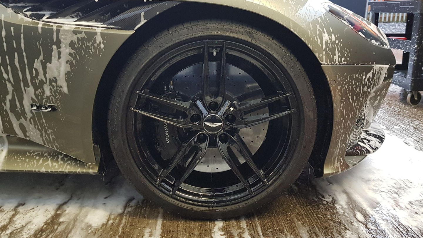 The black wheels of an Aston Martin during the cleaning process, the car is equipped with carbon ceramic brakes.