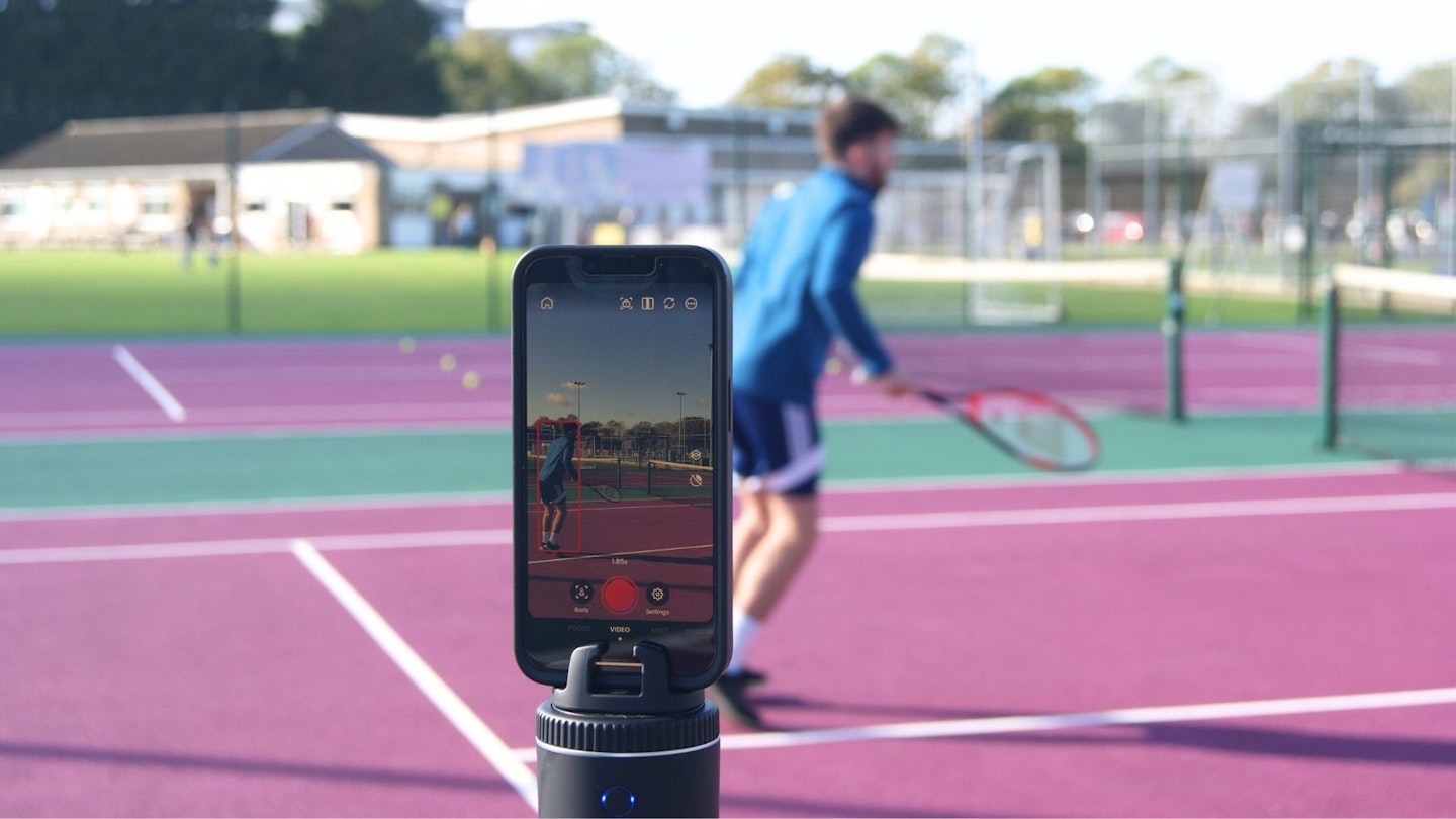 Man playing tennis in background and iPhone and Pivo Pod in foreground. Image credit: Gemma Lavers