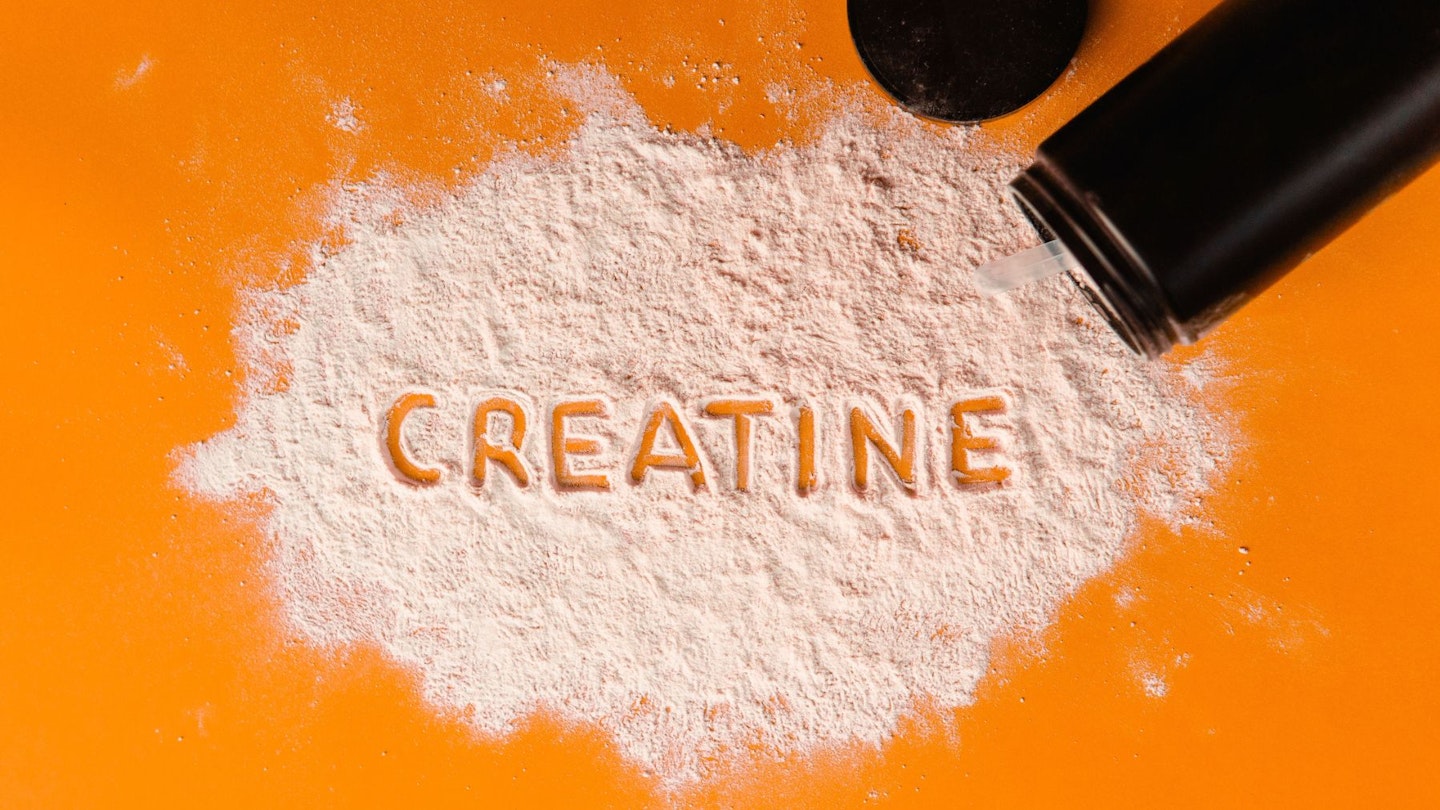 Benefits of creatine for women: 'Creatine' written out with powder on an orange background.