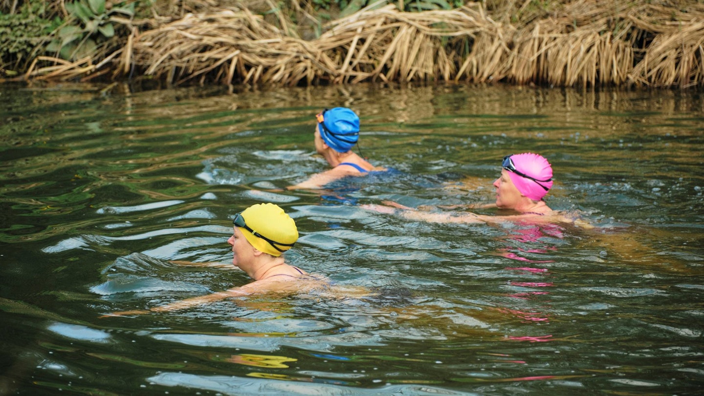 Three women in swimming caps open water swimming